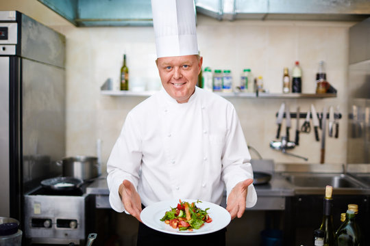 Happy chef with vegetable salad looking at camera