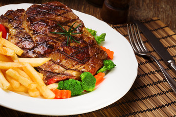 Grilled beef steak served with French fries and vegetables on a