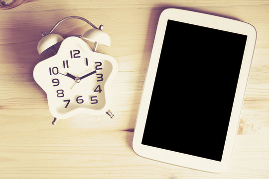 Education concept. Top view Alarm clock on wood table with Tablet PC, vintage tone