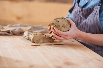 Clay piece holded by hands of woman potter in apron