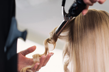 curling woman's hair giving a new hairstyle at hair salon close-up