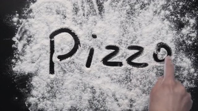 Female cook hand writing "pizza" on the black board with flour. Concept of mediterranean food and culinary. 