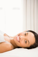 Obraz premium Smiling brunette lying on bed