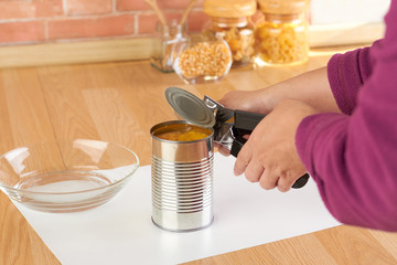 woman opening a can of corn with can opener - obrazy, fototapety, plakaty