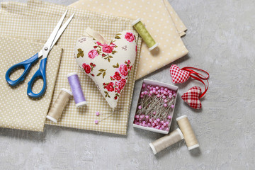 Sewing set: fabrics, threads and pins on pink background