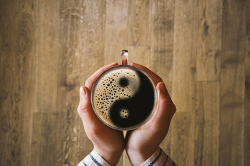 Girl holding a coffee cup with ying and yang symbol. - obrazy, fototapety, plakaty
