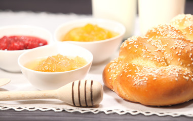 White bowls with homemade jams next to a glass of milk and sweet baked bun are on linen tablecloth on a rustic table
