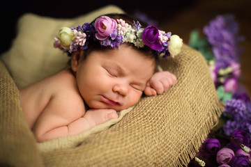 Beautiful newborn baby girl with a purple wreath sleeps in a wicker basket