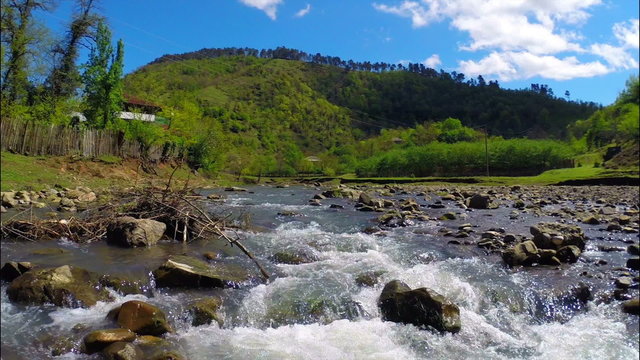 Beautiful view of river flows near village with green forest on the hill under sky with white clouds, Georgia, Guria