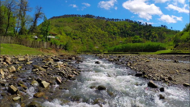 Beautiful view of river flows near village with green forest on the hill under sky with white clouds, Georgia, Guria
