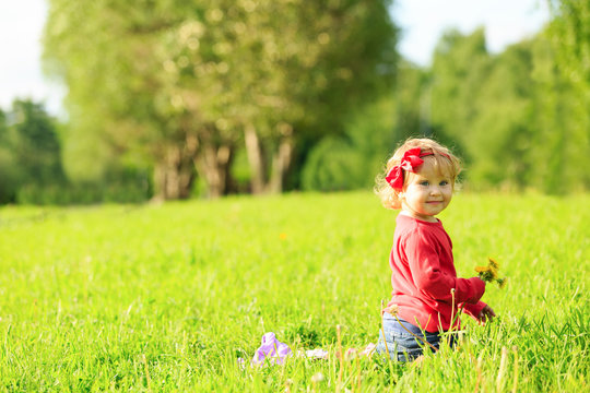 Cute little girl playing with flowers on grass
