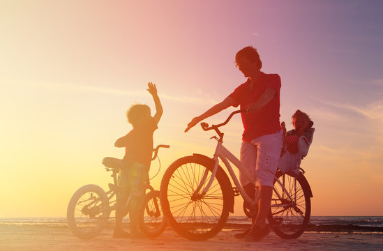 silhouette of father with two kids on bikes
