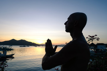 Silhouette of man doing yoga exercises at sunset on the terrace overlooking the ocean - Young person during meditation training - Concept of relaxation with twilight colors and orange filter look