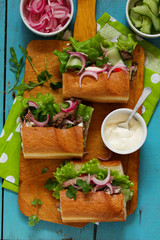 Sandwiches with slices of steak with herbs, vegetables and white sauce.