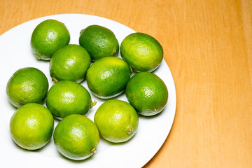Fresh green and yellow limes on a plate over wooden background.