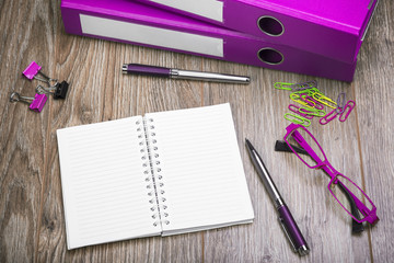 View Of An Office Desk With Ring Binders, Glasses, Notepad And Pen. Workplace With Objects In Color Purple.