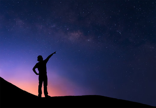 Sillhouette of woman standing next to the milky way and pointing
