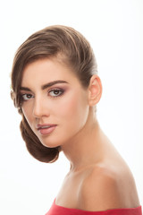 Fototapeta premium Young adorable brunette woman with cute makeup low bun hairstyle in red shirt with bare shoulders looking into camera with curiosity posing on white studio background
