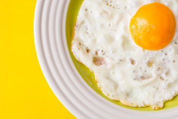 Fried egg on white-green plate on yellow background