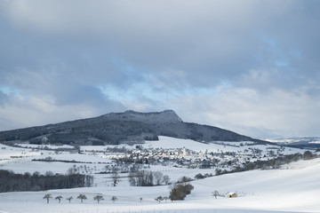 Lichtstimmung in verschneiter Hegaulandschaft, mhlandit dem Hegauvulkan Hohenstoffeln, darunter die Gemeinde Weiterdingen