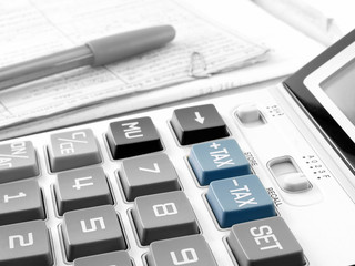 blue tax buttons on white calculator and pen on pile of financial documents