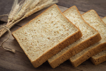 Whole wheat bread slices and wheat on wooden table