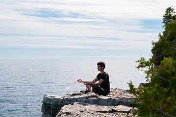 teenage boy sitting on a rock overlooking a lake meditating