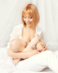 Obraz premium Happy smiling mother feeding breast her baby at home on bed