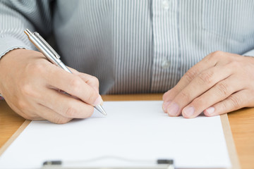 Human hand signing white paper on wood table