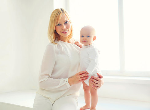 Happy smiling mother with baby home in white room near window