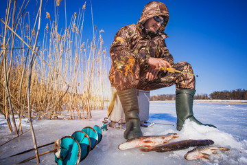 Naklejka premium ice fisherman with pike caught on a tip up