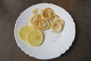 Cooked squid rings with lemon and spices on white dish.