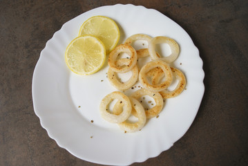 Cooked squid rings with lemon and spices on white dish.