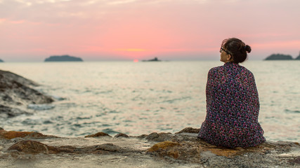Woman wrapped in plaid sits lonely on the coast.