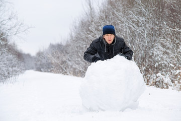 Fototapeta na wymiar Boy rolls a big snowball to build a snowman in winter day