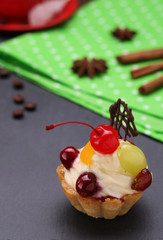 Fruit cake with whipped cream and a cherry on gray background