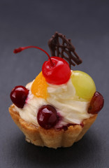 Fruit cake with whipped cream and a cherry on gray background