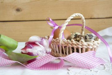 Fototapeta na wymiar Easter eggs with ribbons in a wicker basket, next to the pink tulip.