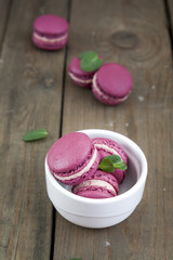 Sweet crimson french macaroons in white plate
and mint on dark wooden background