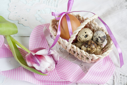 Easter eggs with ribbons in a wicker basket, next to the pink tulip.
