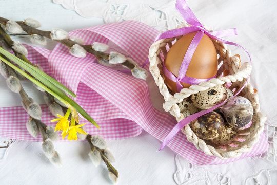 Easter eggs with ribbons in a wicker basket, next to the pussy willow and daffodil (yellow narcissus)