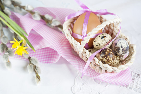 Easter eggs with ribbons in a wicker basket, next to the pussy willow and daffodil (yellow narcissus).