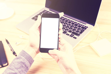 Girl with blank smartphone and opened laptop on wooden table, mo