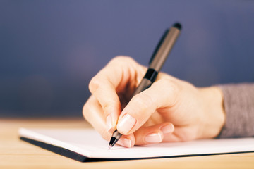 Girl writes notes in diary on wooden table, close up