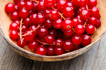 Redcurrant on a branch close to a wooden bowl.