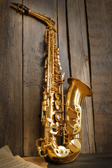 Beautiful golden saxophone with musical notes on wooden background, close up