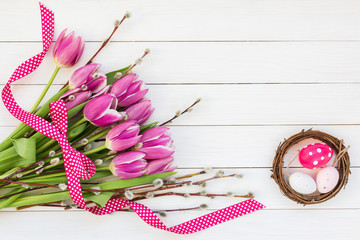 Tulips and decorative Easter eggs in small nest on white table. Top view, copy space 