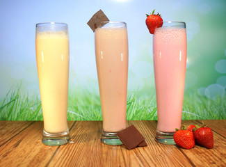 Tres malteadas de diferentes sabores: chocolate, vainilla y fresa, dispuestas sobre un piso de...