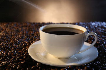 Cup of hot coffee among coffee beans on dark background