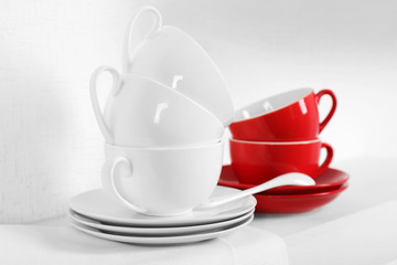 Set of cups and saucers with napkin on shelf against white wall background